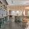 A large community kitchen with an island, dining table, and chairs next to a sunlit bar looking out to a patio at Adara apartments in Downtown Phoenix, AZ.